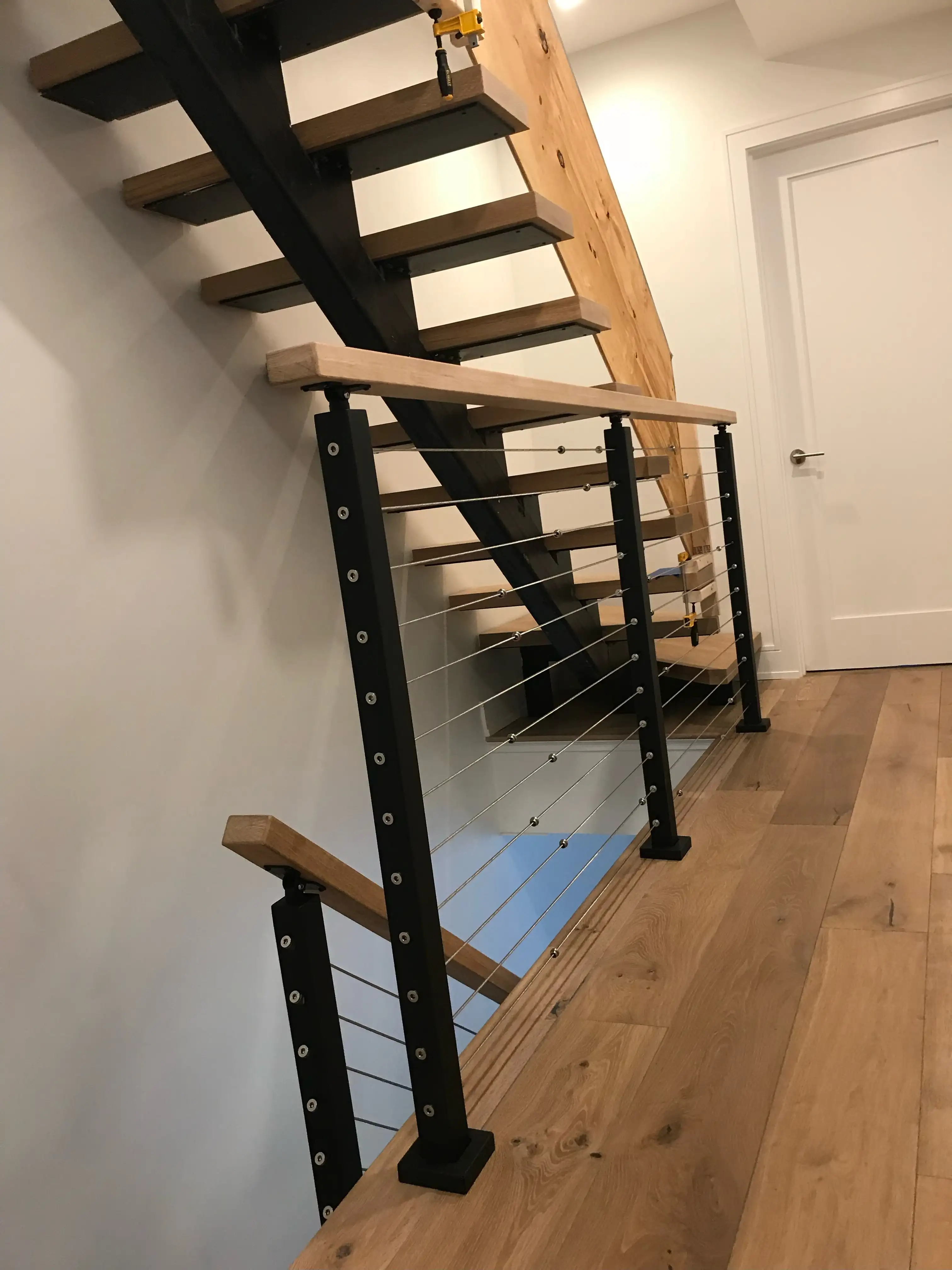 Interior stair guardrail with black steel posts, stainless cable infill and a timber top rail