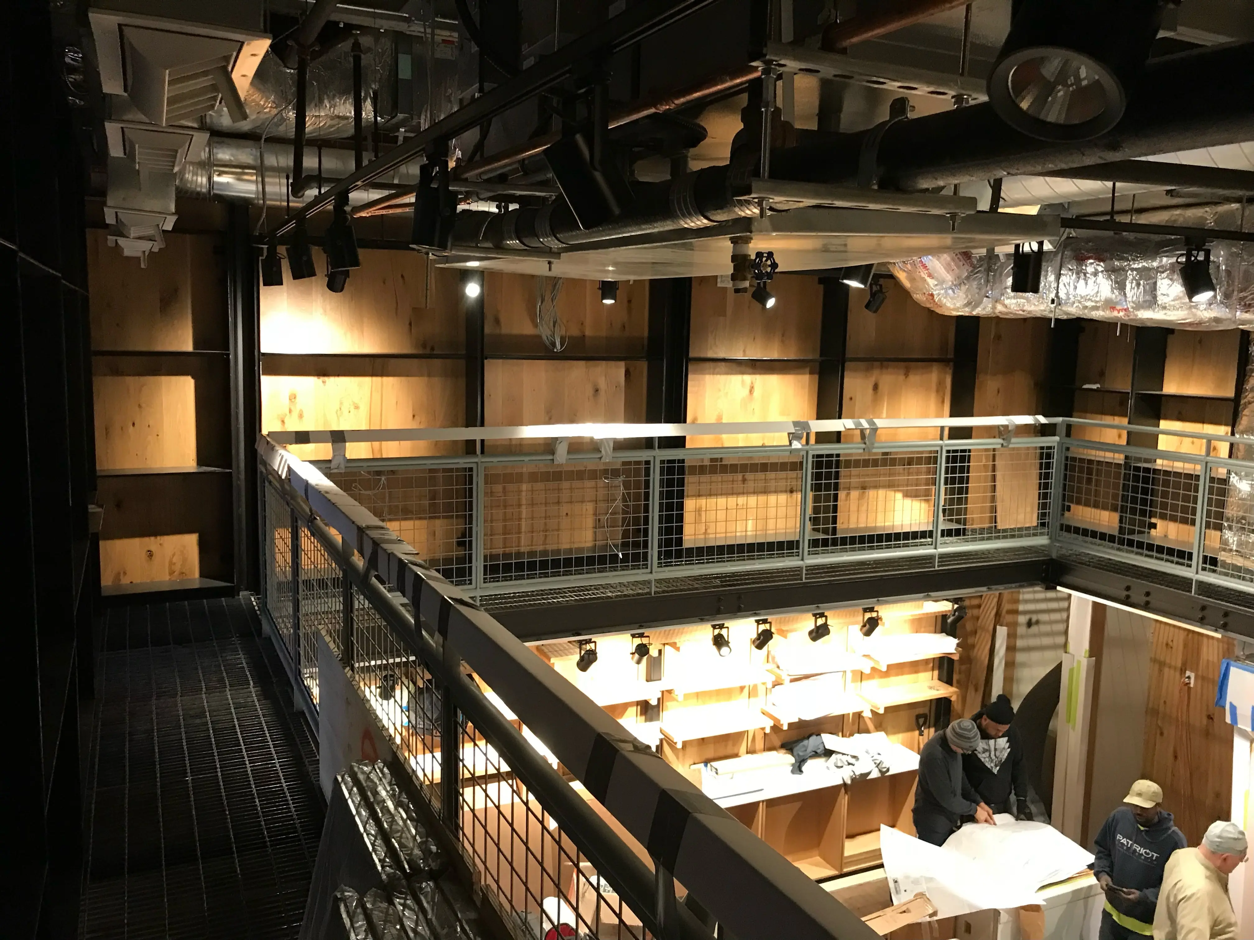 Steel mezzanine catwalk with woven wire mesh guardrail overlooking a timber-clad commercial interior