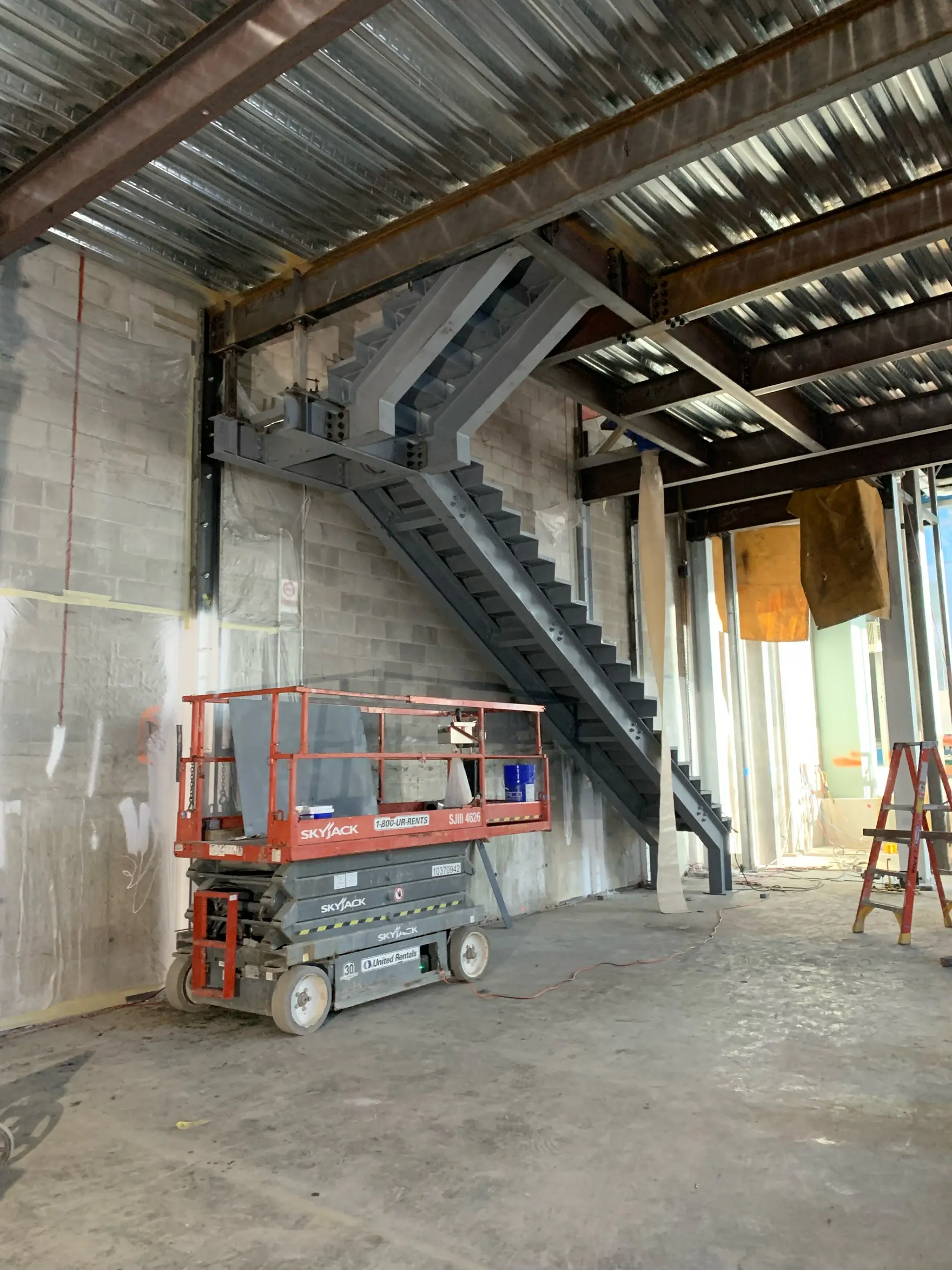 Bare structural steel stair with plate stringers rising to a mezzanine inside a commercial building shell under construction